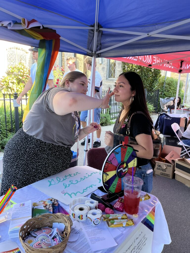 One person applies glitter to a visitor to the table