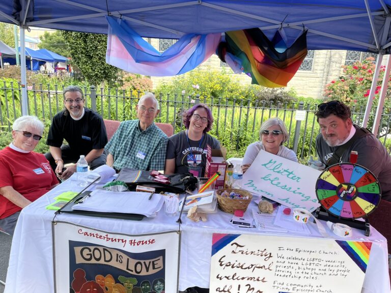 The afternoon shift of volunteers seated at a table covered with sway and welcome signs